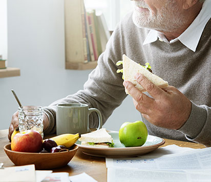 Older man sitting at table eating sandwich